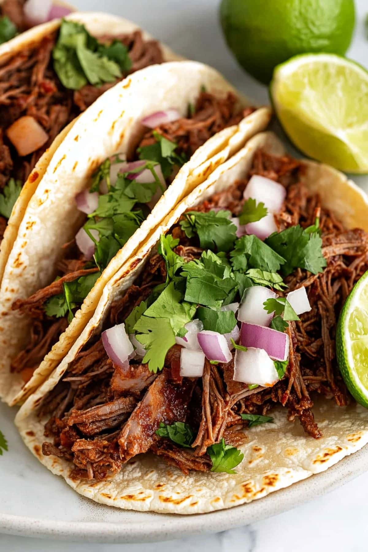 Barbacoa beef served inside taco shells garnished with chopped onions and parsley leaves.