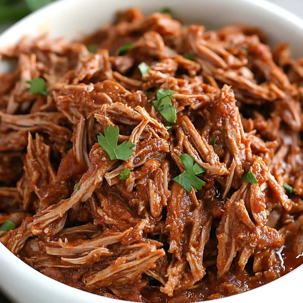 Shredded beef barbacoa in a white bowl.