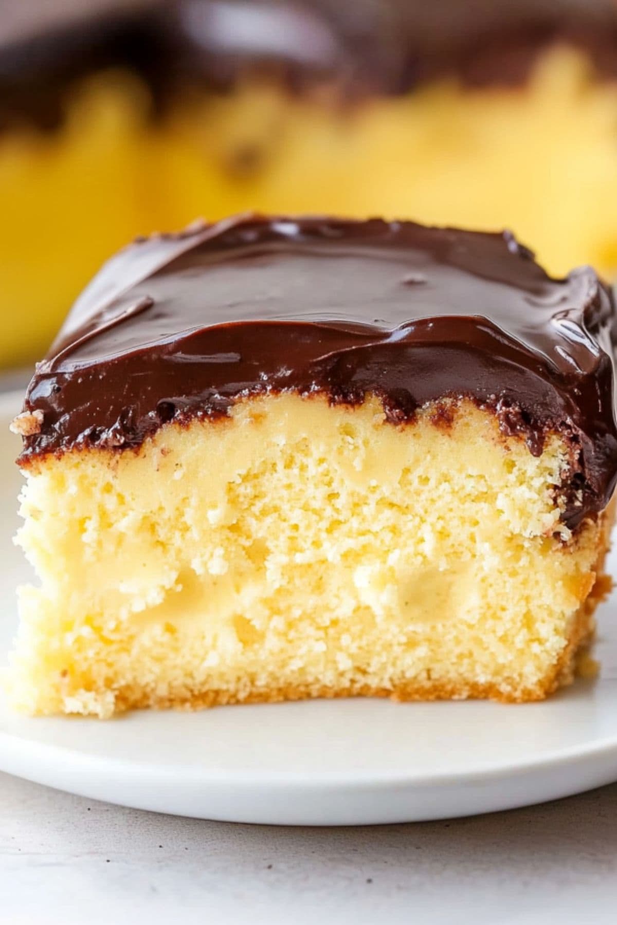 A slice of Boston cream pie poke cake with chocolate ganache served in a white plate.