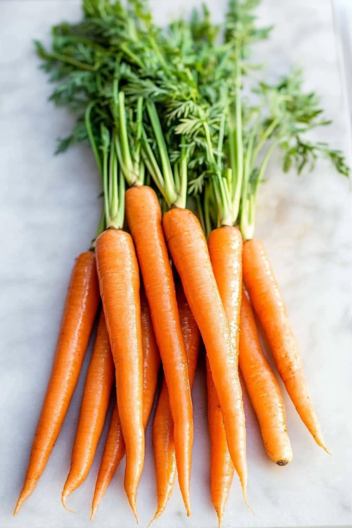 Fresh whole carrots with green top laid out on a white marble countertop.