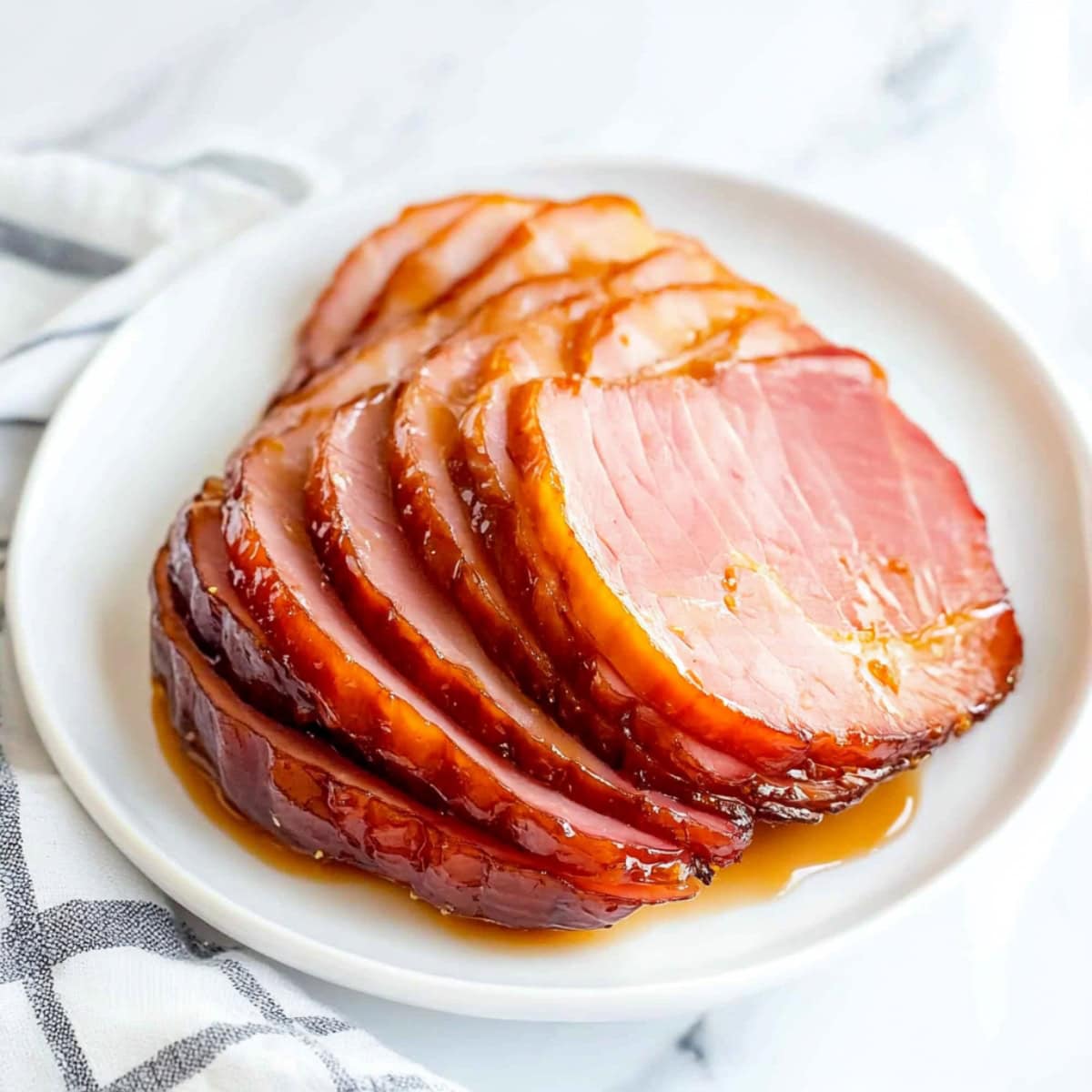 Close-up of a maple glazed ham with caramelized edges, sliced and served on a white plate.