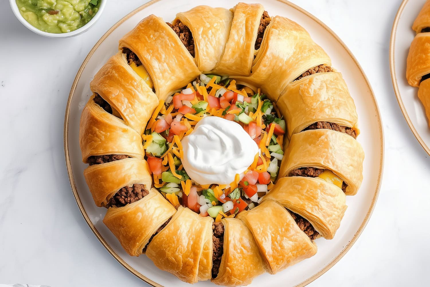 An overhead of taco ring filled with ground beef with colorful veggies and sour cream at the center.