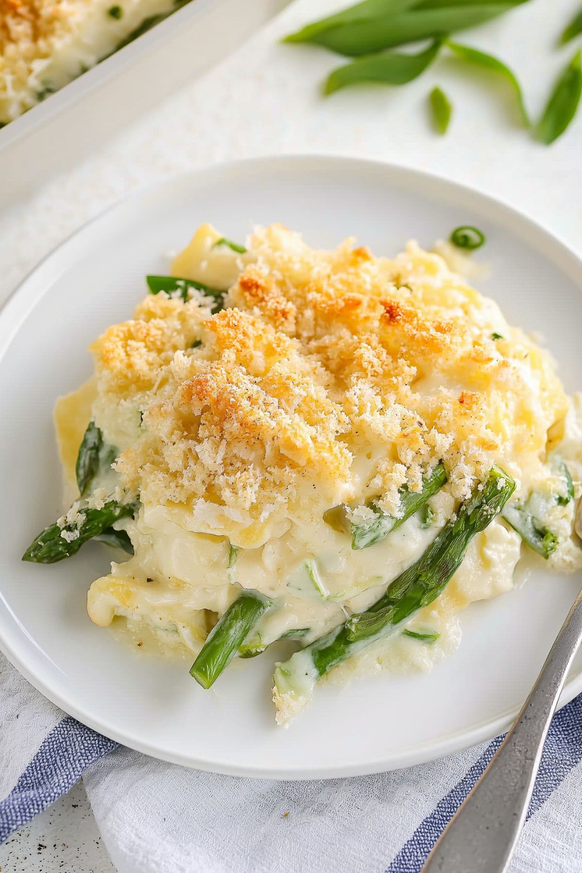 Serving of creamy and cheesy asparagus casserole in a white plate.