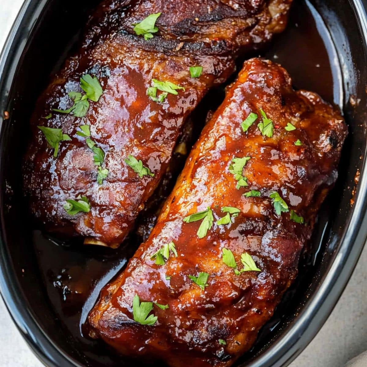 Baby back ribs in a slow cooker pot with barbeque sauce.