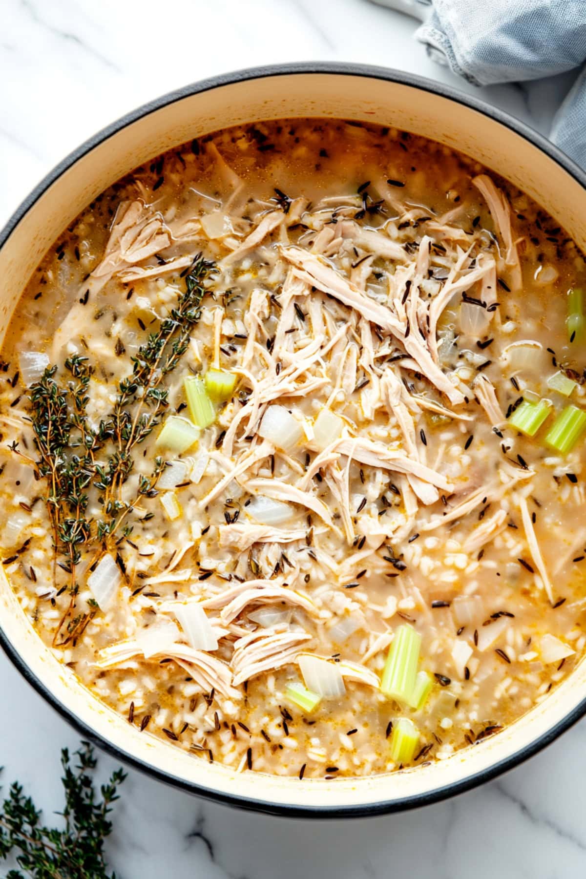 An overhead view of turkey and rice soup with onions, celery and thyme in a large pot.