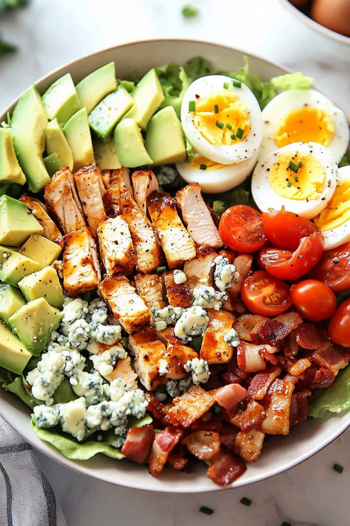 A fresh Cobb salad featuring grilled chicken, crisp bacon, creamy avocado slices, hard-boiled eggs, cherry tomatoes, blue cheese crumbles, and a bed of mixed greens.