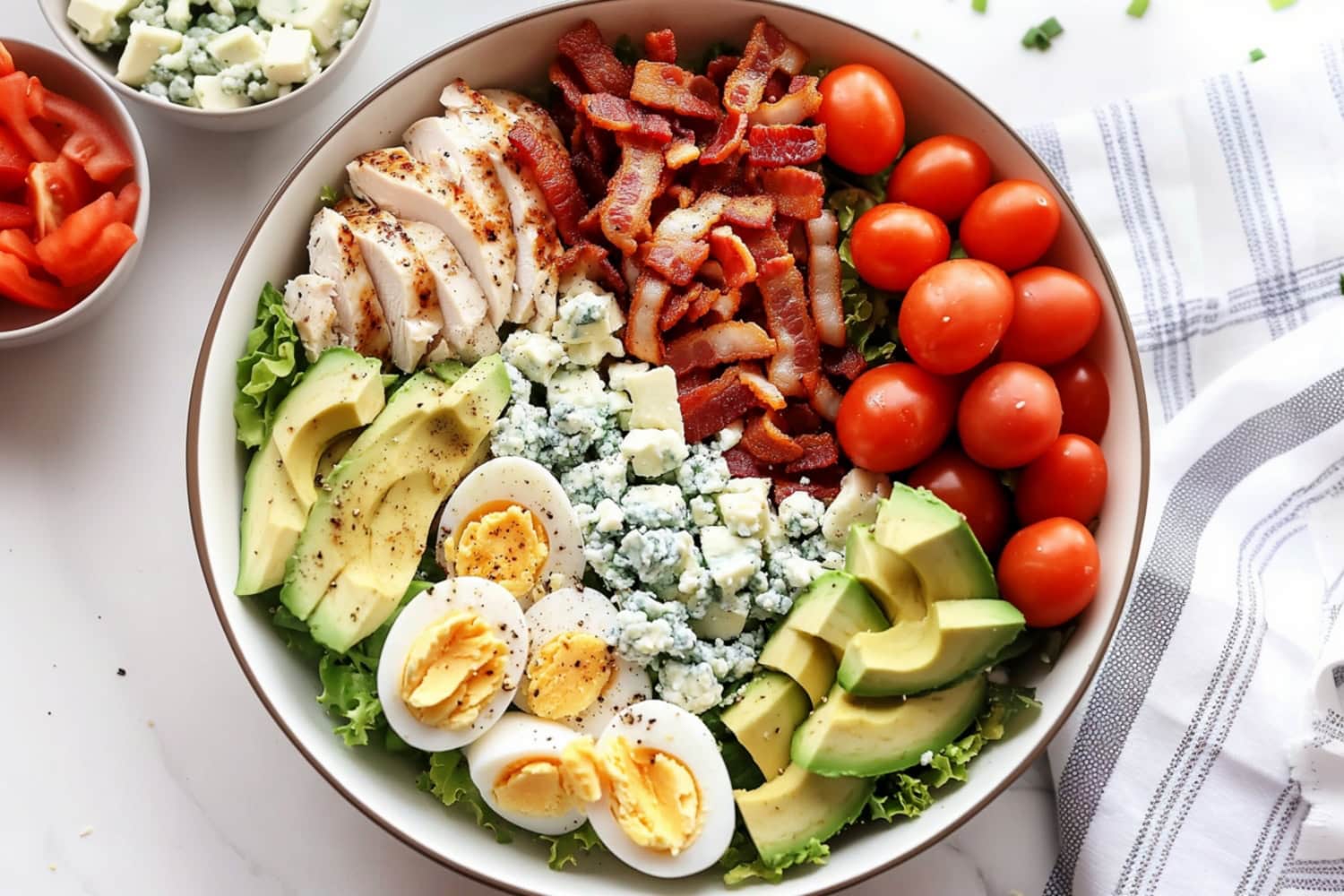 A healthy Cobb salad full of bright colors: grilled chicken, ripe avocado, chopped bacon, halved boiled eggs, and juicy tomatoes over a bed of romaine lettuce.