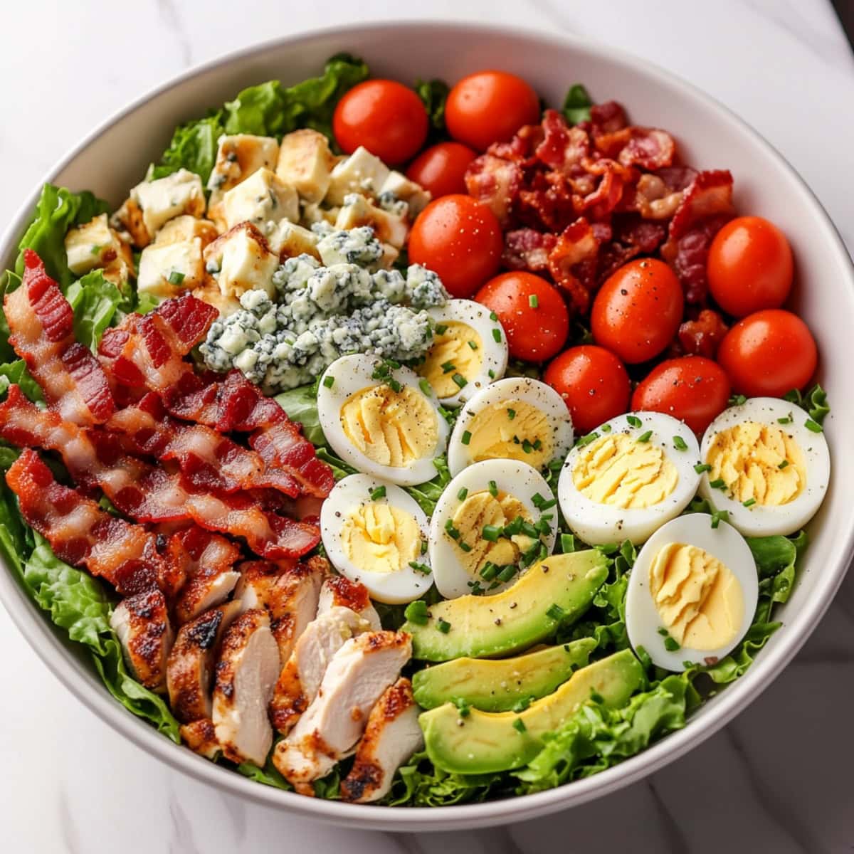 A bowl of salad featuring hard boiled eggs, chicken, tomatoes and bacon.