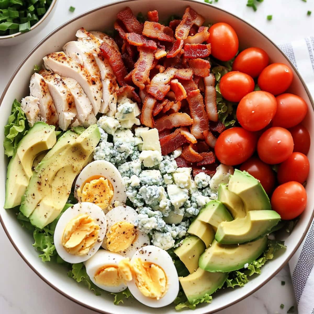 A neatly arranged Cobb salad, with layers of diced chicken, crispy bacon bits, sliced eggs, avocado wedges, and fresh greens.